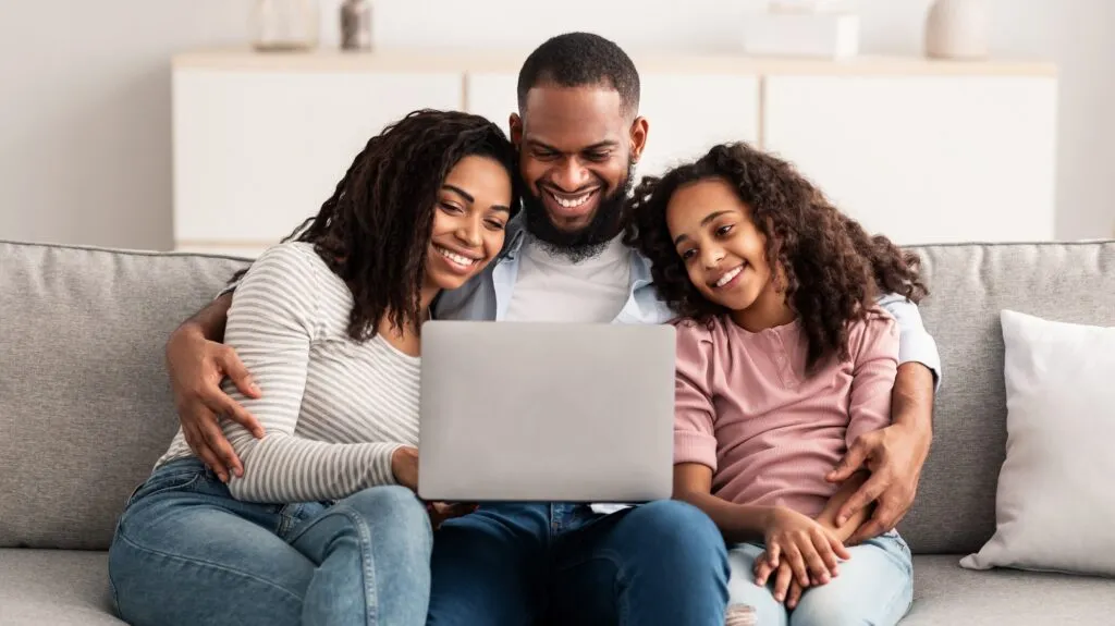 Happy African American family using laptop on sofa. Parents and daughter enjoy family time together. Lewisville, TX.