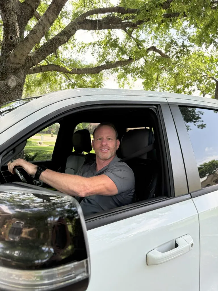 Man in a white truck, ready to go. A driver is behind the wheel, smiling. Home in Lewisville, TX, is where he is headed.