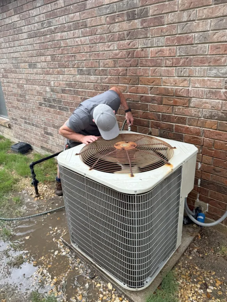 HVAC technician inspecting an AC unit outside a home. Air conditioning maintenance in Lewisville, TX. Home cooling system repair.